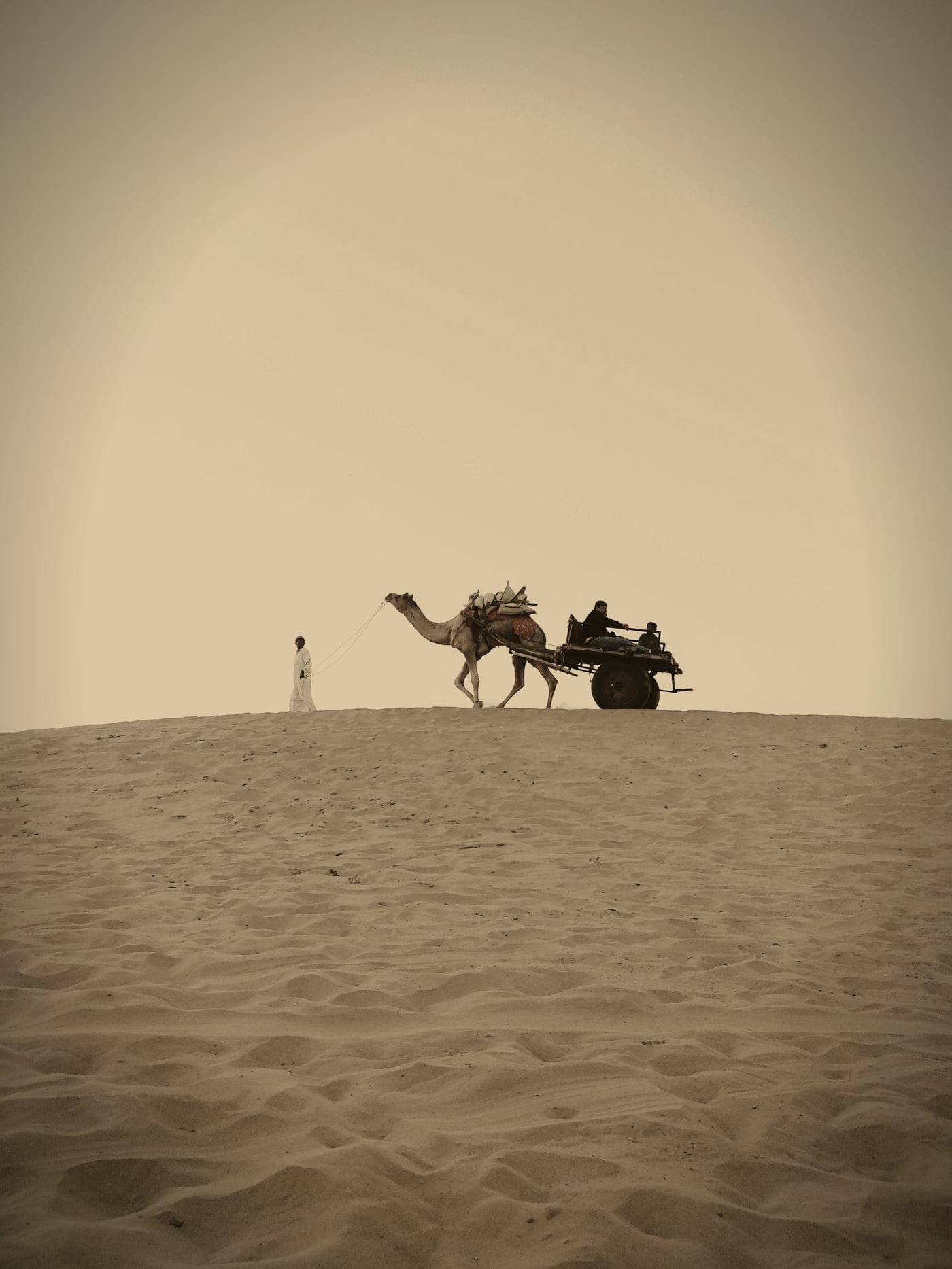 A lone camel cart crossing the crest of a sand dune near Jaisalmer