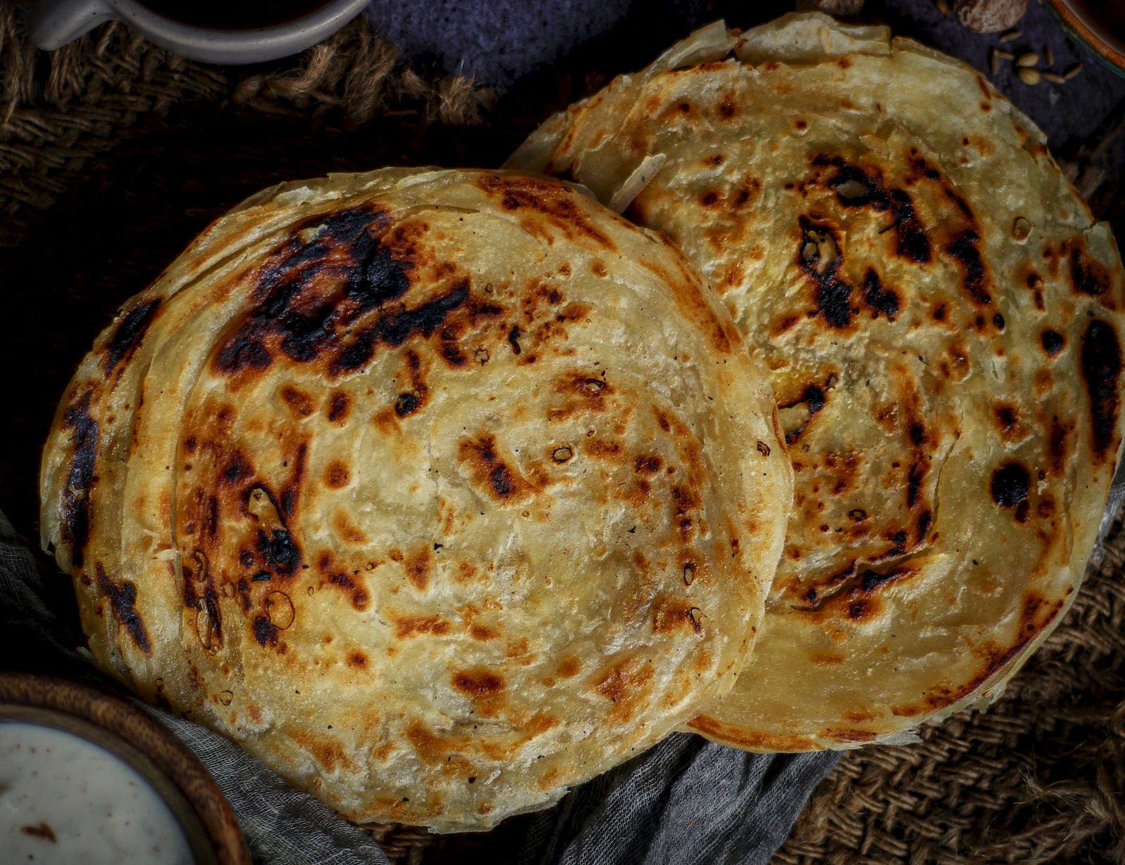 Two layered flatbreads with charred spots and crisp edges, resting on dark linen