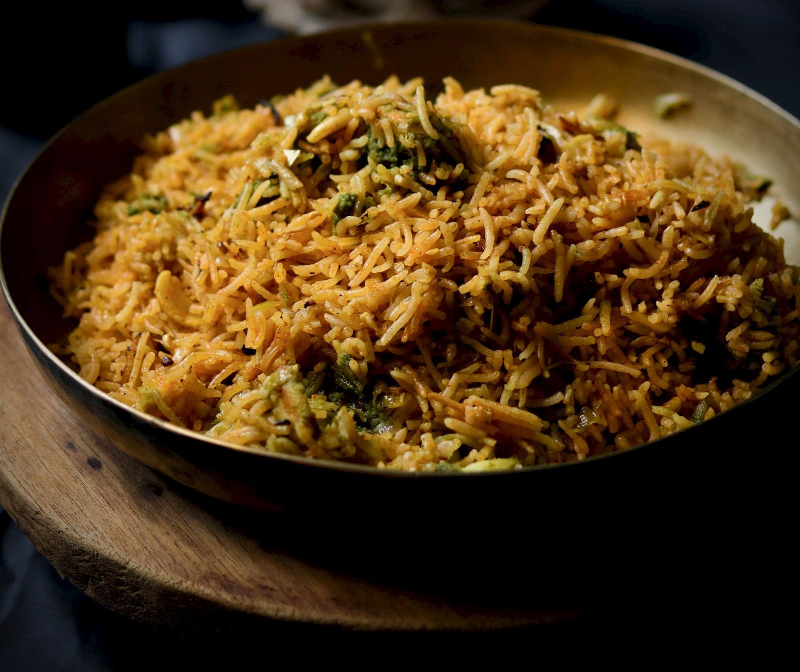 Pulao with whole spices in a shallow brass dish, lit low from the side