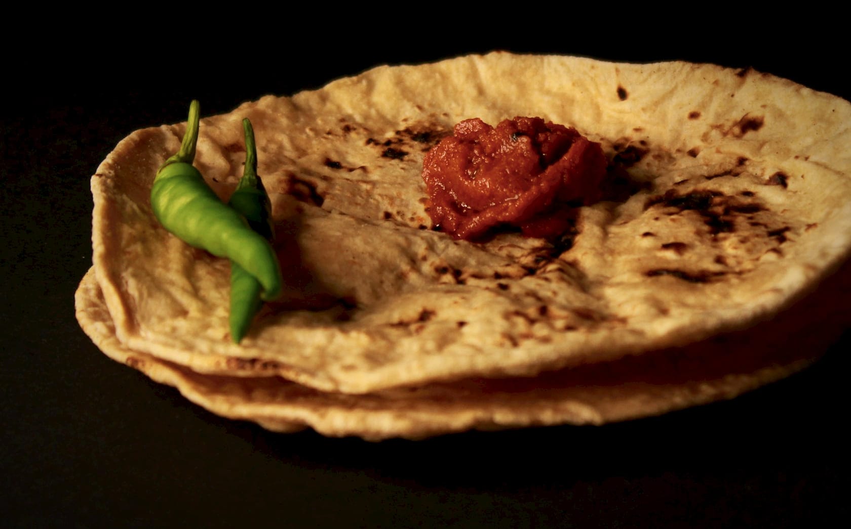 Lightly blistered whole wheat rotis, stacked, with a green chilli