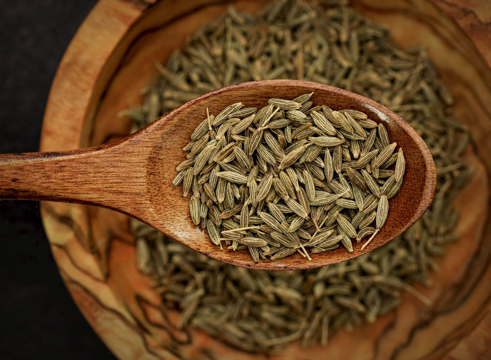 Cumin seeds heaped in a carved wooden spoon over a bowl of cumin