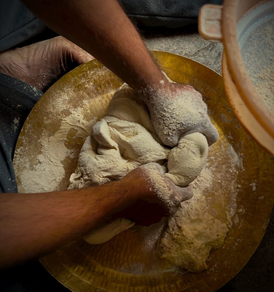Hands kneading dough on a hammered brass paraat dusted with flour